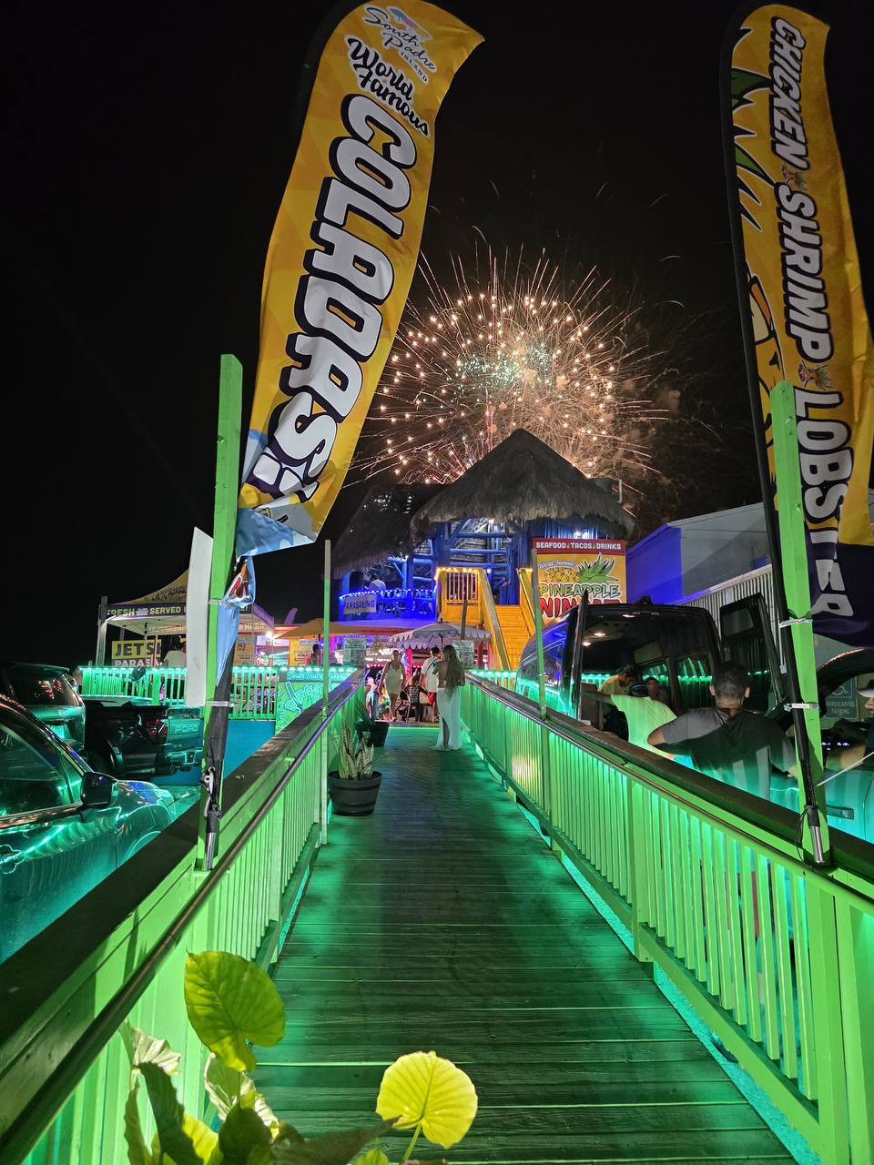 Pineapple Ninjaz on South Padre Island lit up green at night with fireworks over the waterfront palapa